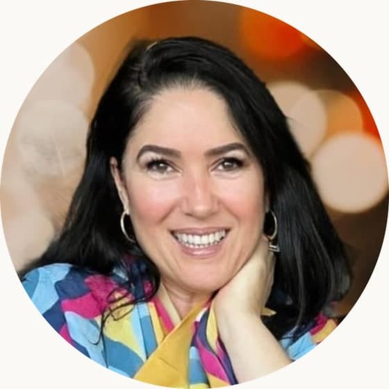 Adrianna Kezh, sorrindo, apoiada em uma mesa de madeira.